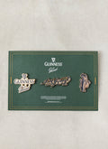 The Guinness x Percival 3 Pack Pins displayed on a green presentation card, featuring gold-tone metallic enamel pin badges.