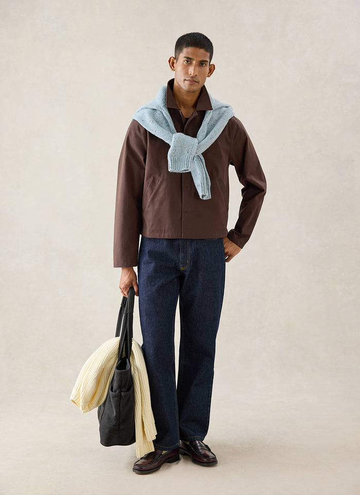 A model wears the espresso Percival Carter Cropped Jacket, styled with dark denim jeans and a light blue jumper.