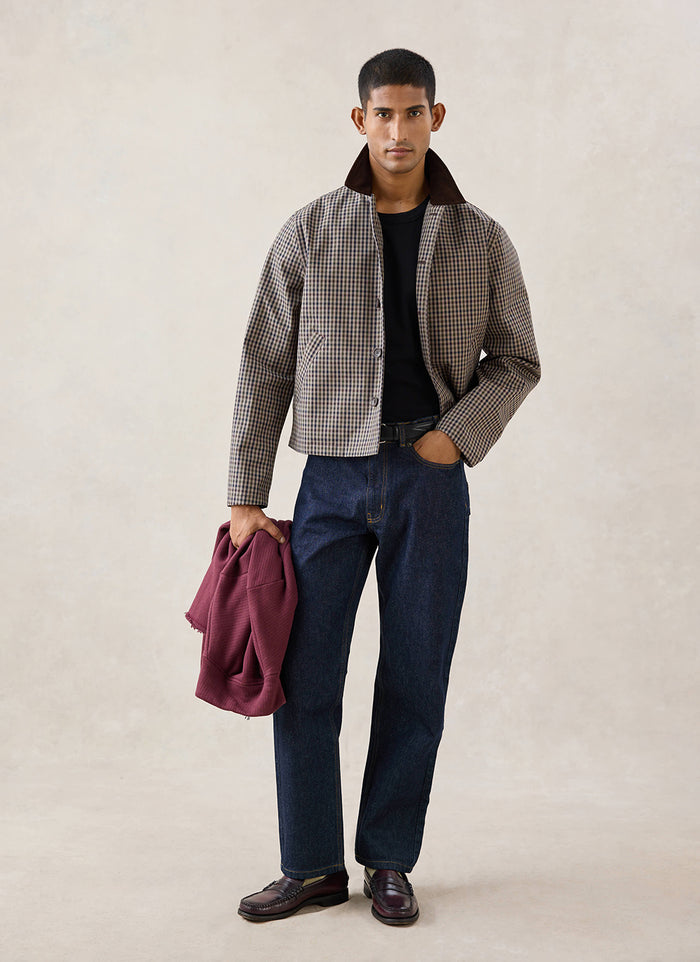 A model wears the Watcher Check Percival Carter Cropped Jacket with blue jeans and loafers in a studio shot.