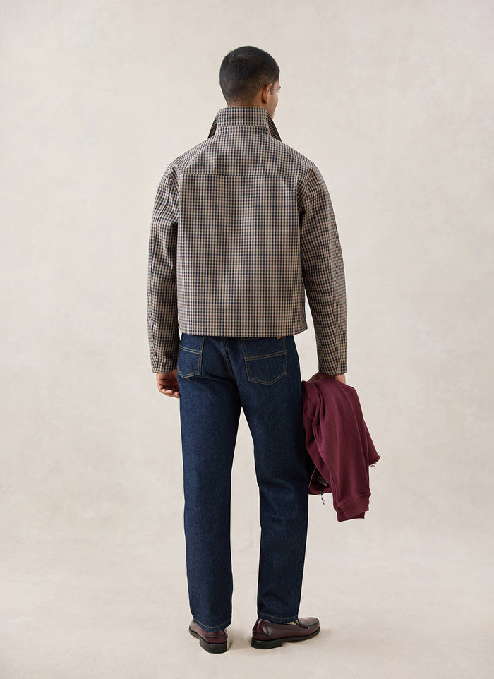 A rear-view shot of a model wearing the Watcher Check Percival Carter Cropped Trench Coat, styled with dark denim jeans.