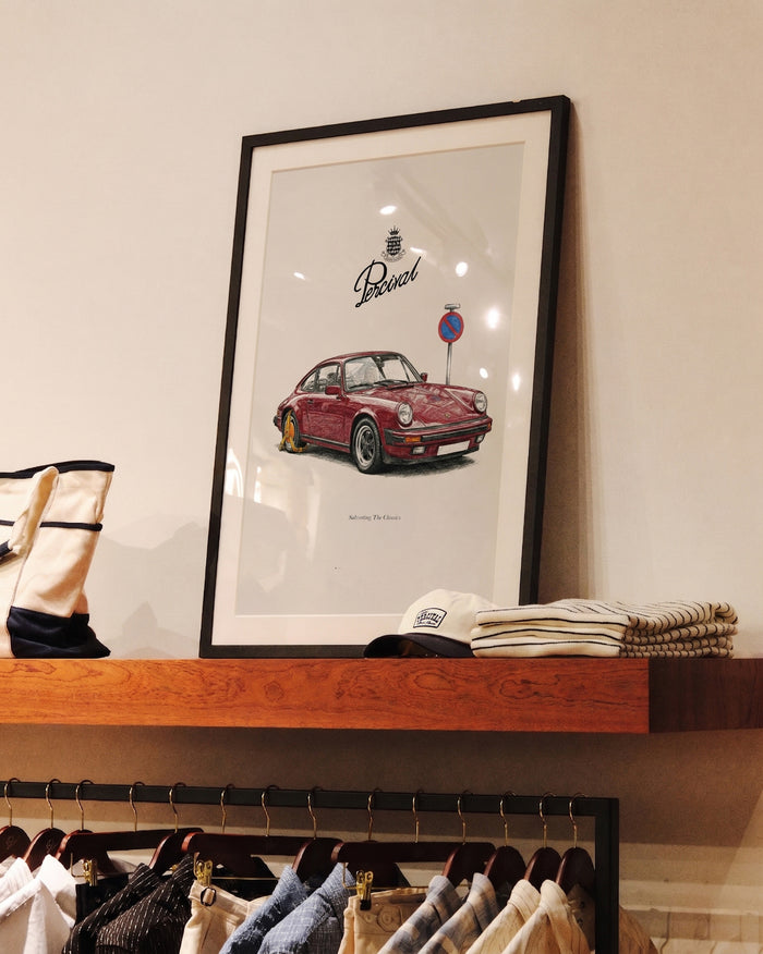 A framed Clamped Porsche fine art print by Percival, displayed on a wooden shelf in store.