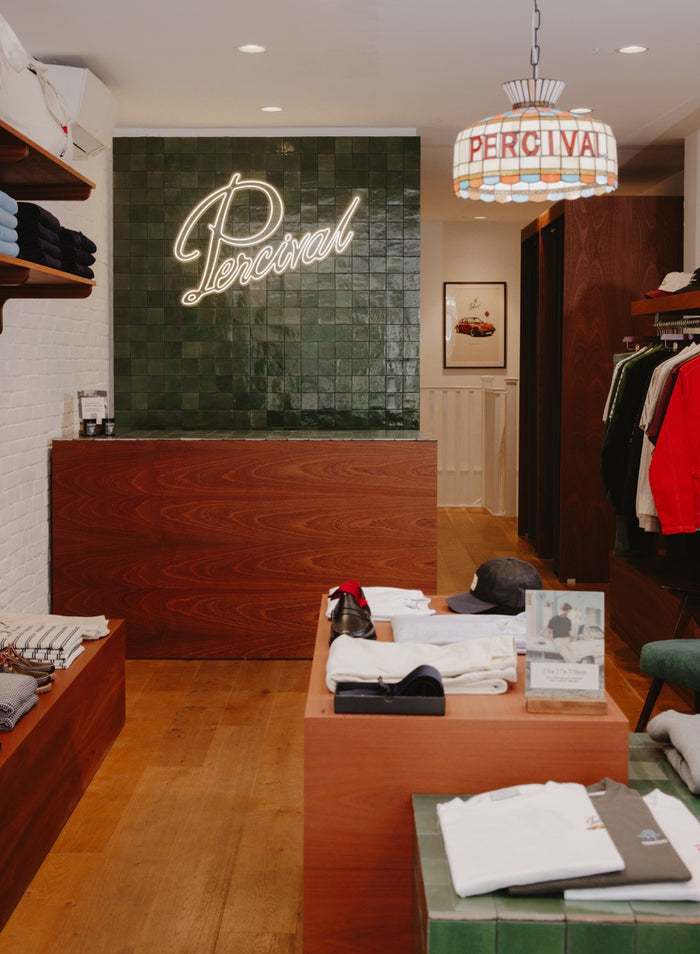 Inside a Percival store featuring a neon logo on a green tiled wall and a framed print in the background.