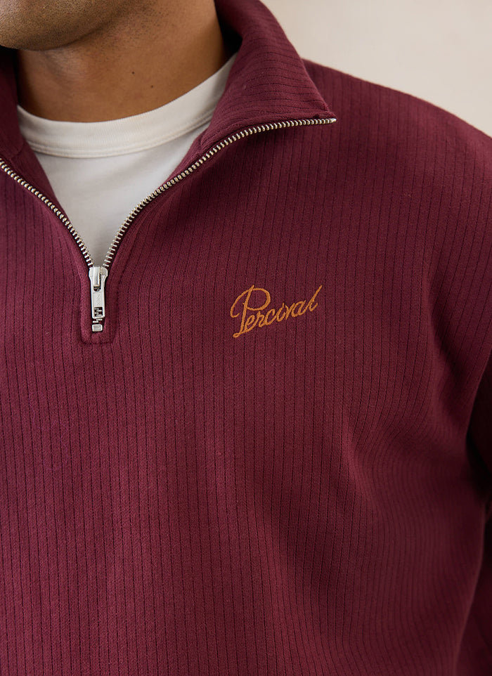 Close-up of a burgundy Percival Conrad 1/4 zip jumper in cotton, showing the ribbed texture and zipper detail.