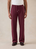 A model wears the merlot Percival Conrad straight leg trackpants, styled with a white t-shirt and dark loafers.