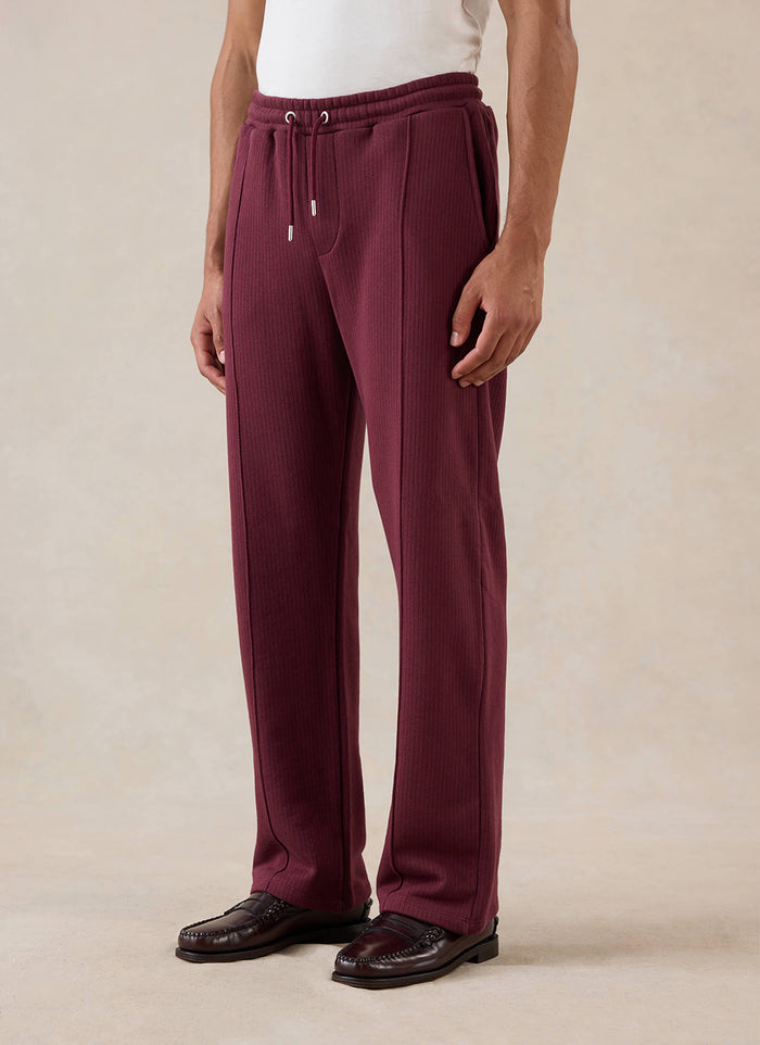 A model wears the merlot Percival Conrad Straight Leg Trackpants with a white t-shirt and loafers in a studio shot.