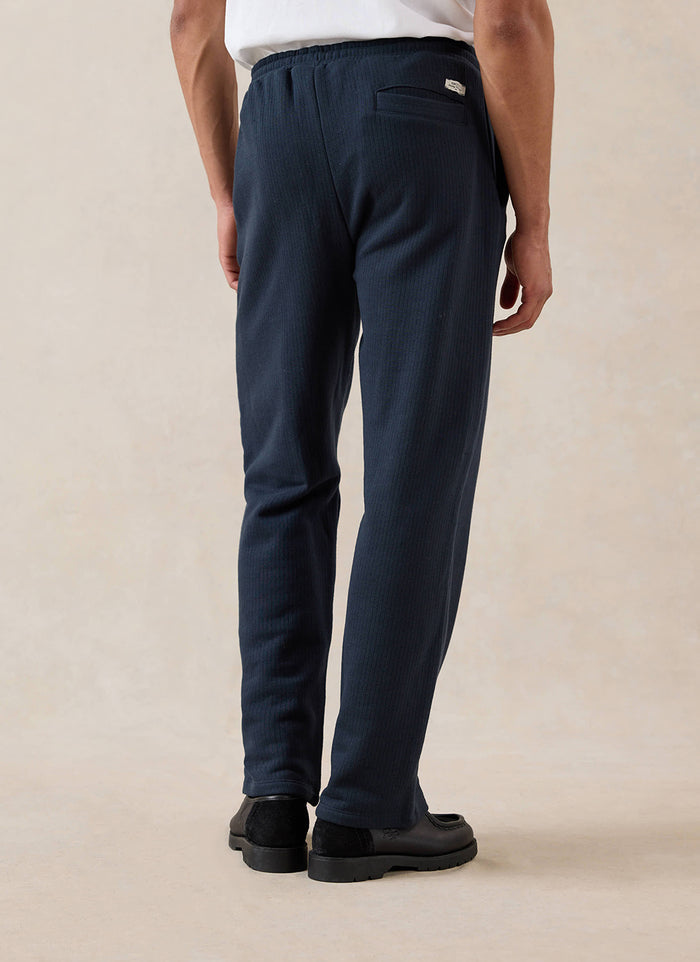 Rear view of a model wearing navy Percival Conrad straight leg trackpants.