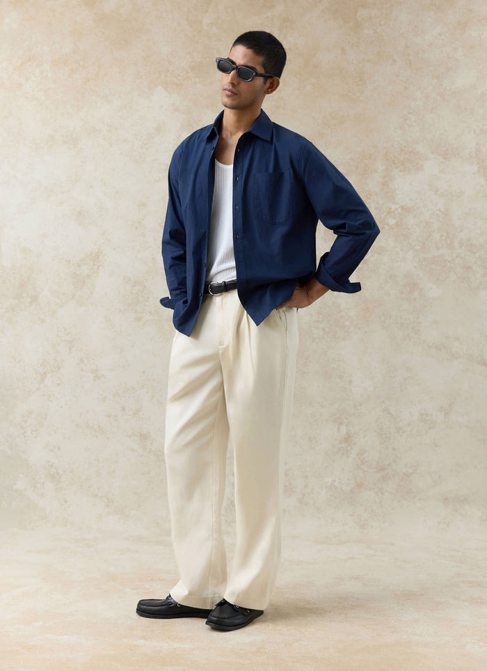 Navy cotton Percival Dali Relaxed Poplin Shirt, styled open over a white vest and cream trousers on a model.