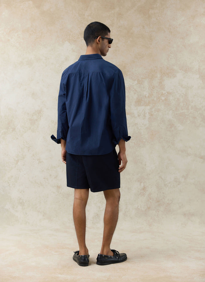 Back view of the navy cotton Dali Relaxed Poplin Shirt by Percival, featuring a back yoke and box pleat detail.