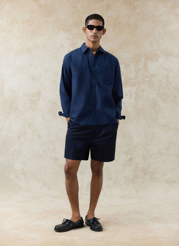 Navy Percival Dali Poplin Shirt and matching Blake Double Pleated Shorts worn by a model against a textured backdrop.