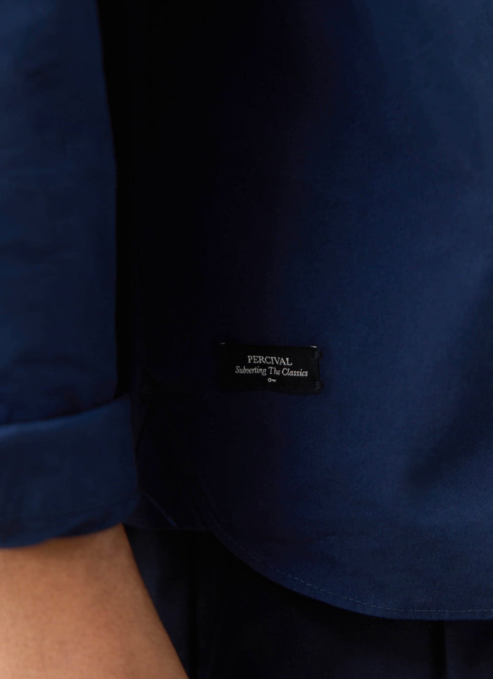 Close-up of the navy cotton Percival Dali Relaxed Poplin Shirt, featuring the Subverting The Classics hem label.