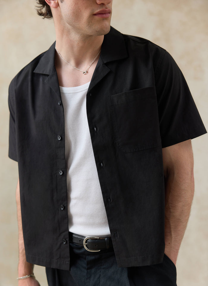 Black cotton Percival Daniel Boxy Cuban Shirt, styled with a white vest and SS26 trousers. Want more? Check out the range.