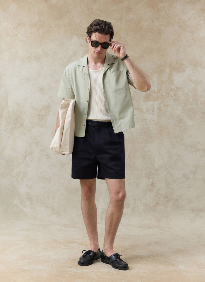 Percival Daniel Boxy Cuban Shirt in pistachio cotton, styled on a model with black shorts and a cream tote bag.