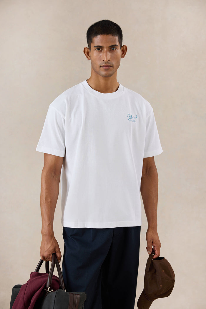 A model wears the white Percival Dawson boxy t-shirt, styled with dark trousers and accessories in a studio setting.