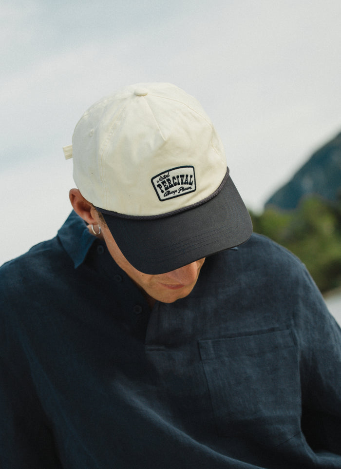 Cream Percival Donovan Soft Trucker Cap featuring a contrast navy brim, rope detail, and an embroidered motel patch.