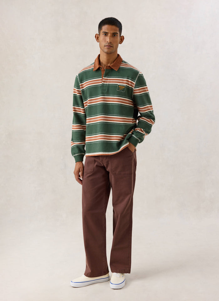 Model wearing the Guinness x Percival striped rugby polo in forest green, featuring a cord collar and chest patch.