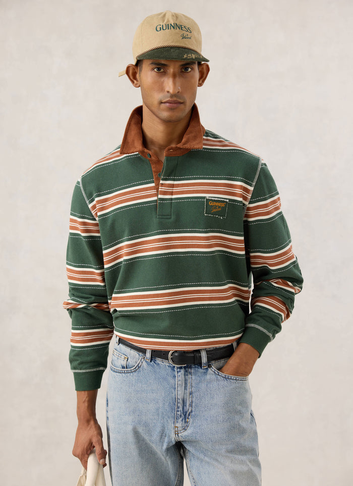 Model wearing the Guinness x Percival striped rugby polo shirt in forest green with a brown corduroy collar.