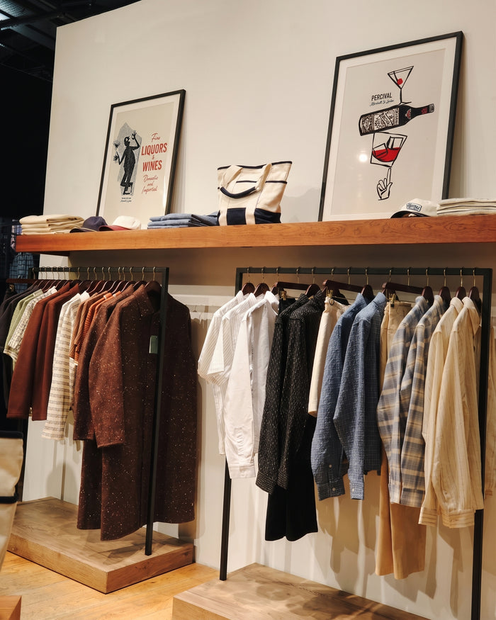 Two Percival framed prints displayed on a shop shelf above clothing racks in a store.