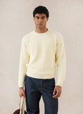 A model wears the cream Percival Fisherman Raglan Jumper, styled with dark denim jeans in a studio shot.
