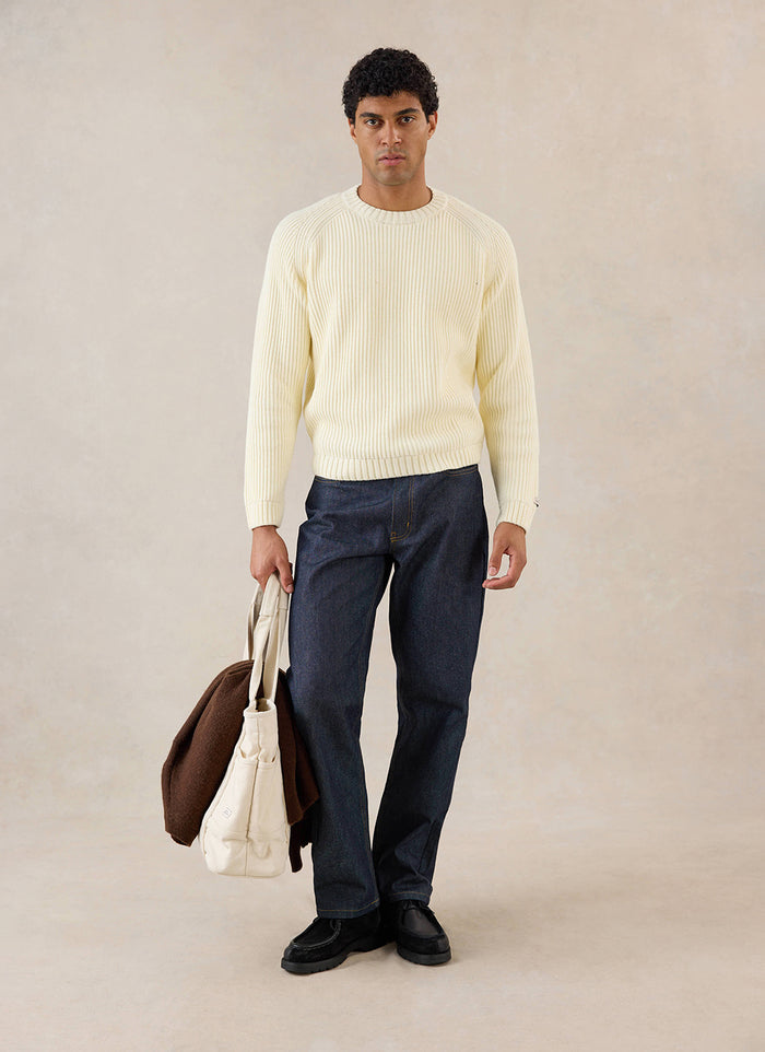A model wears the cream Percival Fisherman knitted jumper, styled with dark jeans and holding a canvas tote bag.