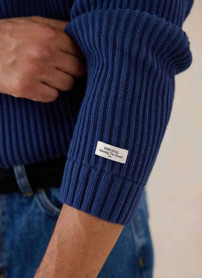 Close-up of a model wearing the navy Percival Fisherman Knitted Jumper, highlighting the textured ribbing and branding label.