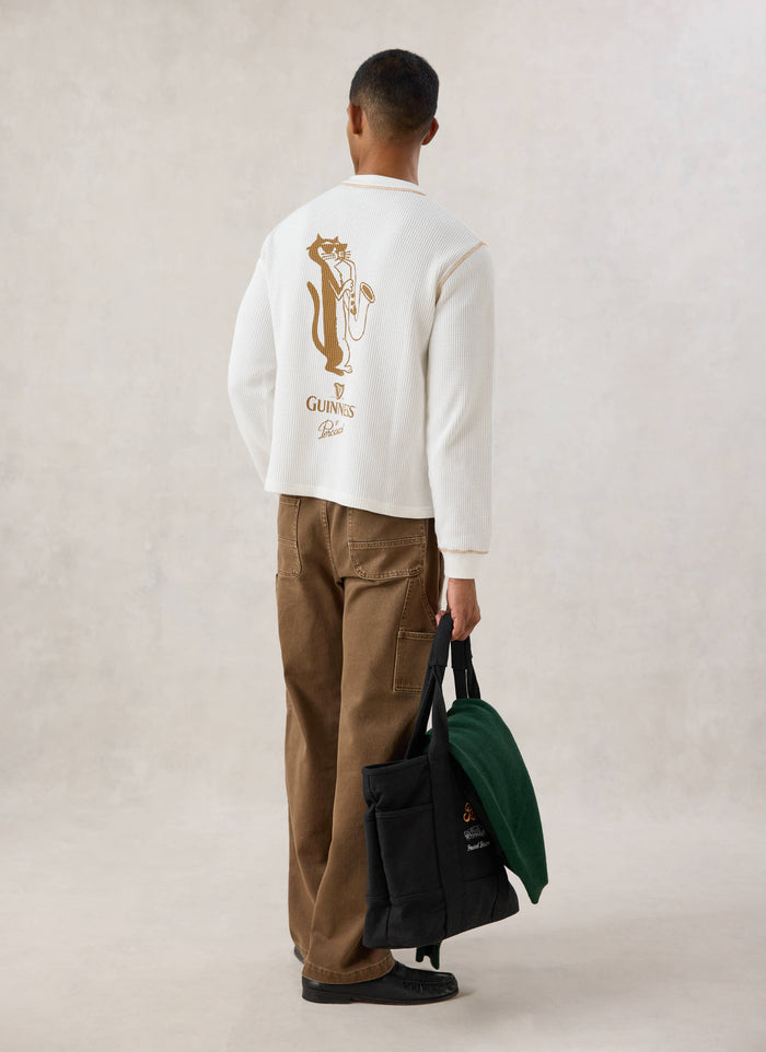 Rear view of a model wearing the Guinness x Percival cream waffle henley long sleeve t-shirt, showing the back cat graphic.