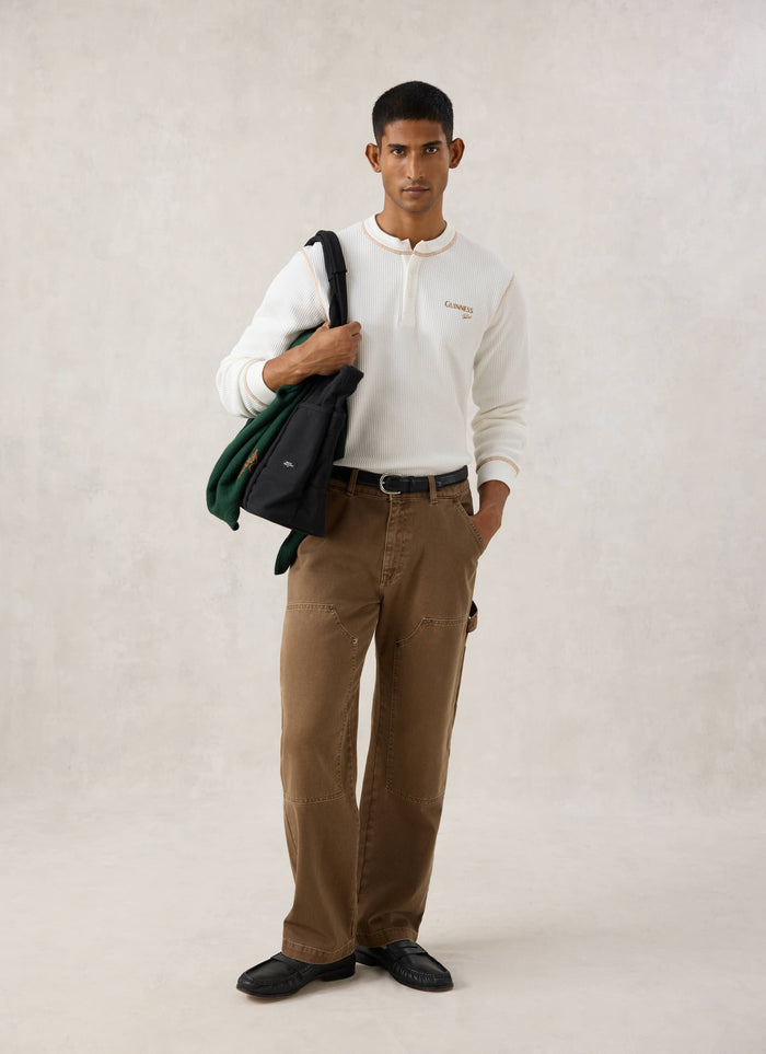 Model wearing the cream Guinness x Percival waffle henley with brown trousers and a black bag over his shoulder.