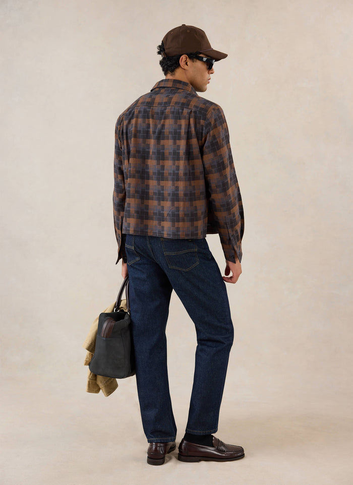 A model seen from behind wears the brown check Hinsley boxy long sleeve shirt from Percival with dark jeans and loafers.
