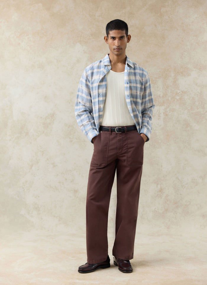 Percival Lungo Herringbone Straight Trousers in espresso cotton, styled with a blue checked shirt and white ribbed vest.