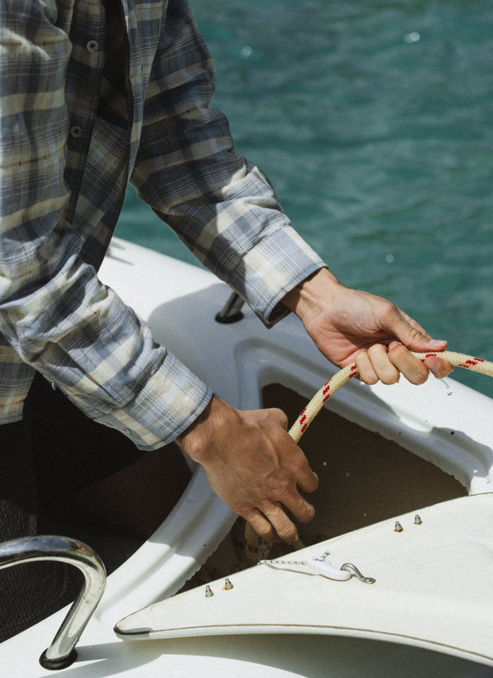 The blue check Percival Jesse cropped shirt, a breathable linen-cotton blend, worn while handling a rope on a boat.