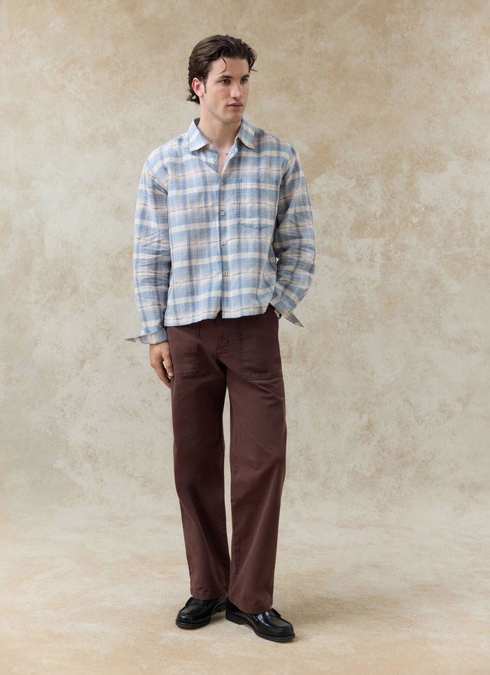 Percival Jesse Cropped Shirt in light blue check, a boxy linen-cotton blend shirt styled with dark brown trousers.