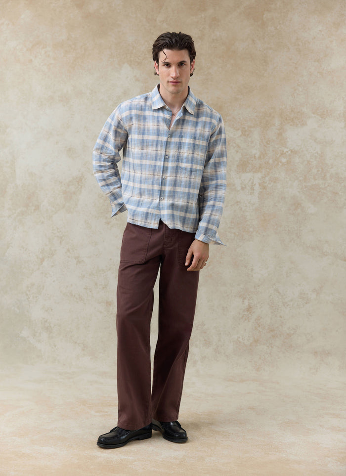 The Percival Jesse Cropped Shirt in a blue check linen-cotton blend, worn by a model with brown trousers.