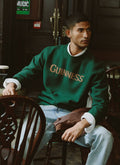 Model wearing the Guinness x Percival forest green merino wool jacquard jumper while sitting inside a pub.