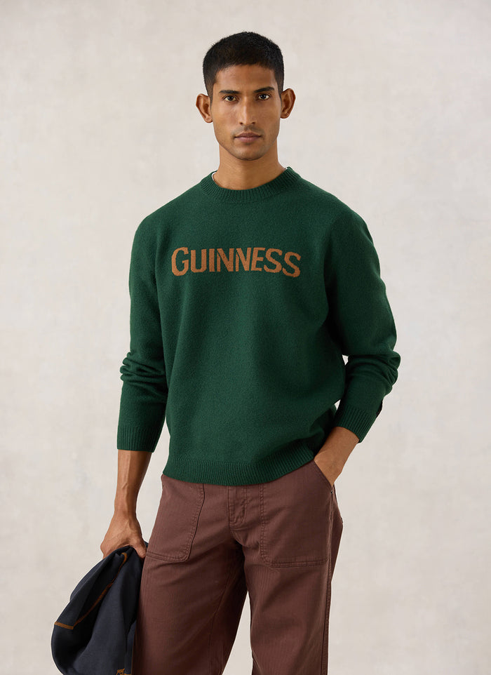 Model wearing the Guinness x Percival forest green merino wool jumper, featuring the bold contrasting jacquard chest logo.
