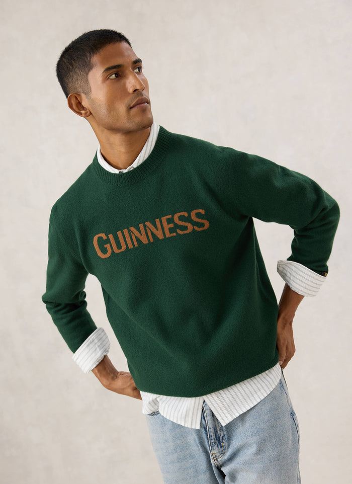 Model wearing the Guinness x Percival forest green merino wool jumper with bold jacquard lettering across the chest.