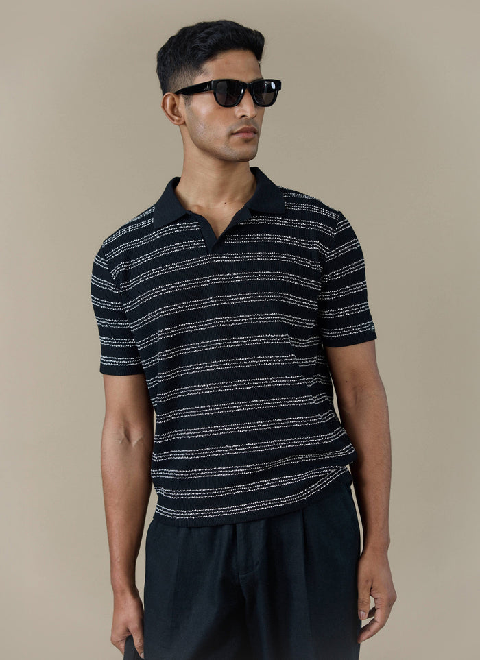 A model wearing the Percival Laurent Polo in black stripe, featuring a boxy fit and textured knit stitch.