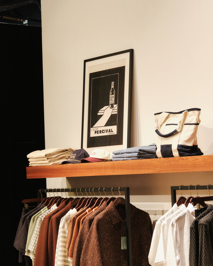 The Liquor Print framed in black, displayed on a wooden store shelf in a Percival store.
