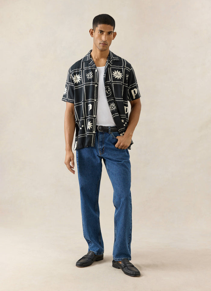 Percival Lunar Panel Cuban Shirt in black viscose with white celestial prints, styled with blue jeans on a model.