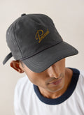 Close-up of a model wearing the charcoal Luther soft trucker cap by Percival, showing the embroidered logo.