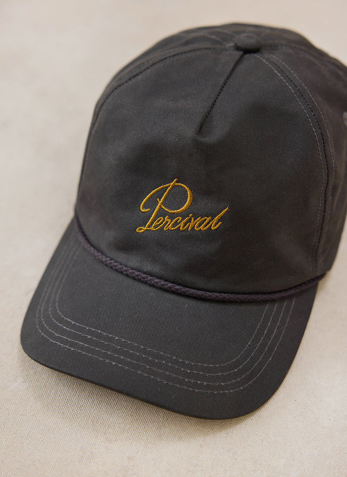 Close-up of the charcoal Percival soft trucker cap in brushed cotton, showing the gold embroidered lettering on the front.