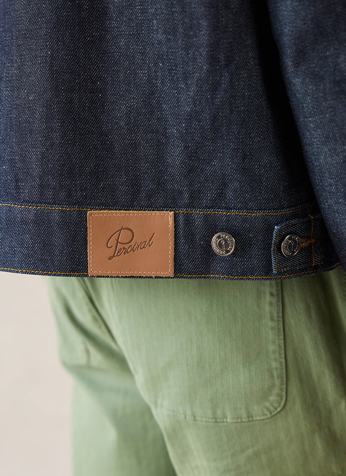Close-up of the leather brand patch and metallic buttons on the raw denim Mackey Zip Jacket from Percival.