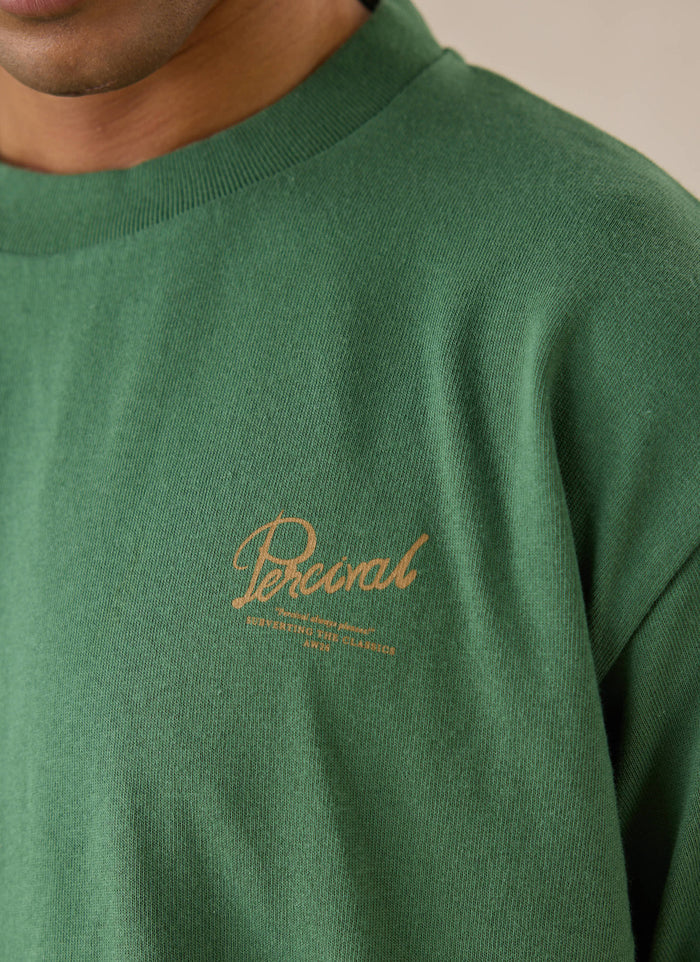 A close-up of the forest green Percival Marley boxy t-shirt, showing the chest branding.