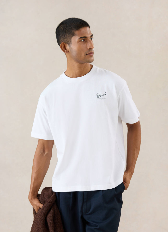A model wears the white Percival Marley boxy t-shirt, showing the chest embroidery in a studio shot.