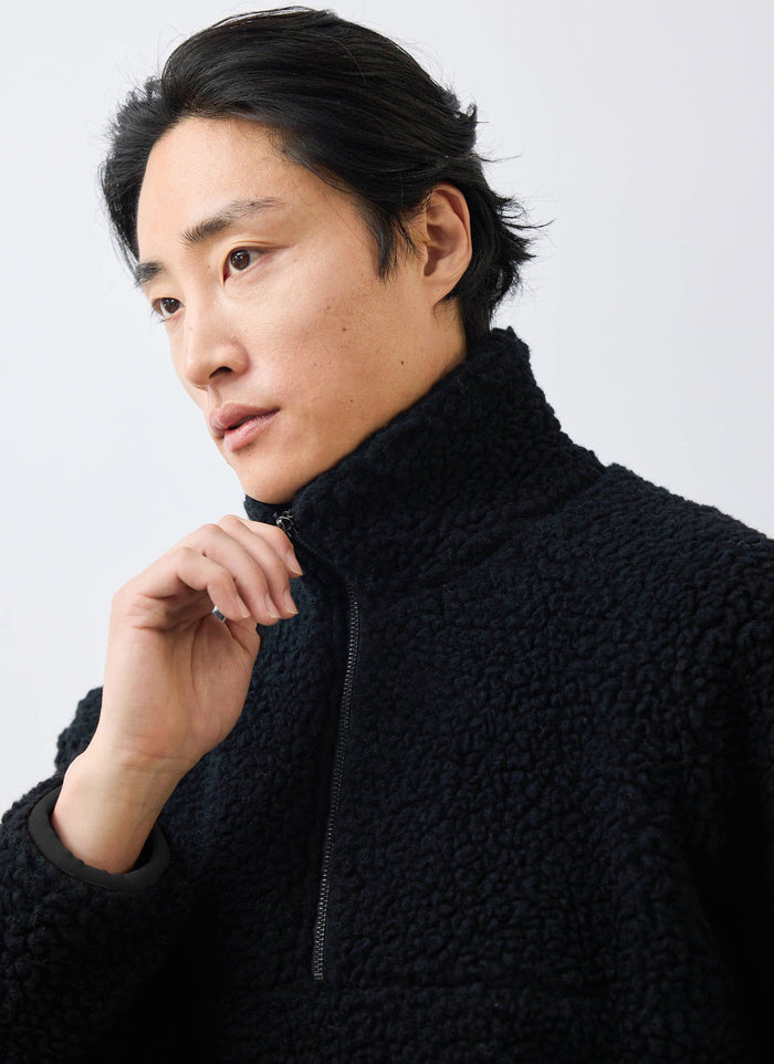 A close-up of a model wearing the black Percival Quarter Zip Wool Fleece Pullover, adjusting the high collar zip.