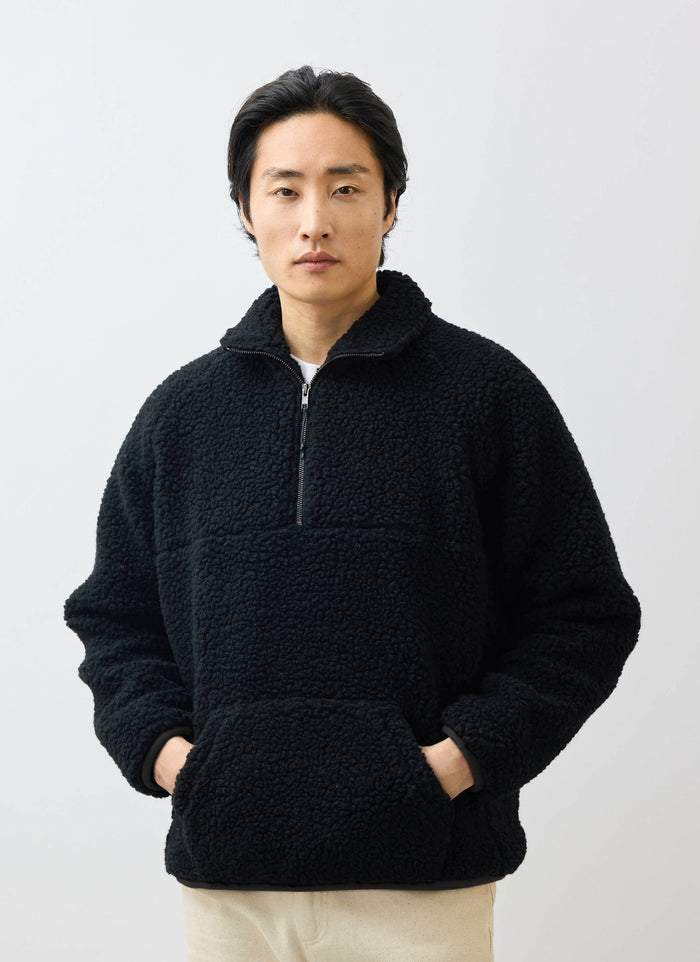 A model wears the Percival black Quarter Zip Wool Fleece Pullover, standing with his hands in the front kangaroo pocket.