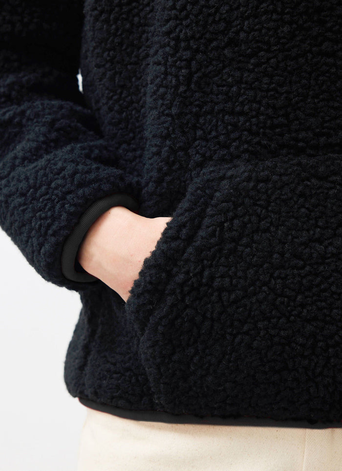 A close-up shot of the Percival Quarter Zip Wool Fleece in black, showing the texture and pocket detail with a hand inside.
