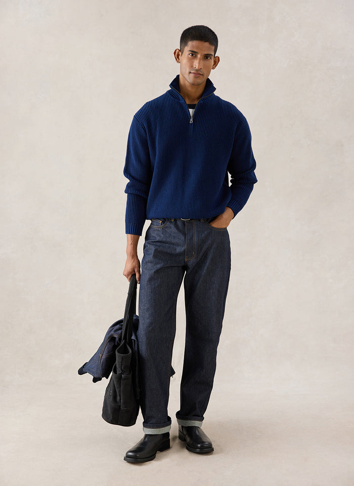 A model wears the navy Meyer Boxy Quarter Zip from Percival with dark jeans, holding a bag in a studio.