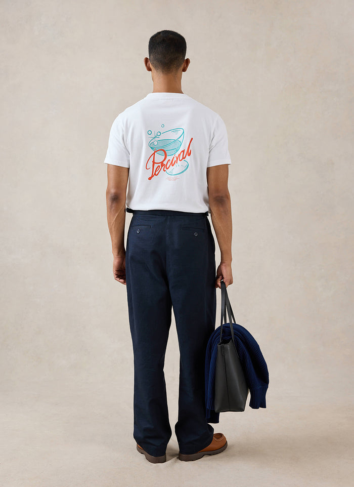 White Percival Norman T-shirt with a cocktail back graphic, worn from behind by a model with dark trousers and a tote bag.
