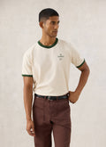 Model wearing the cream Guinness x Percival ringer T-shirt featuring forest green contrast trim and chest branding.
