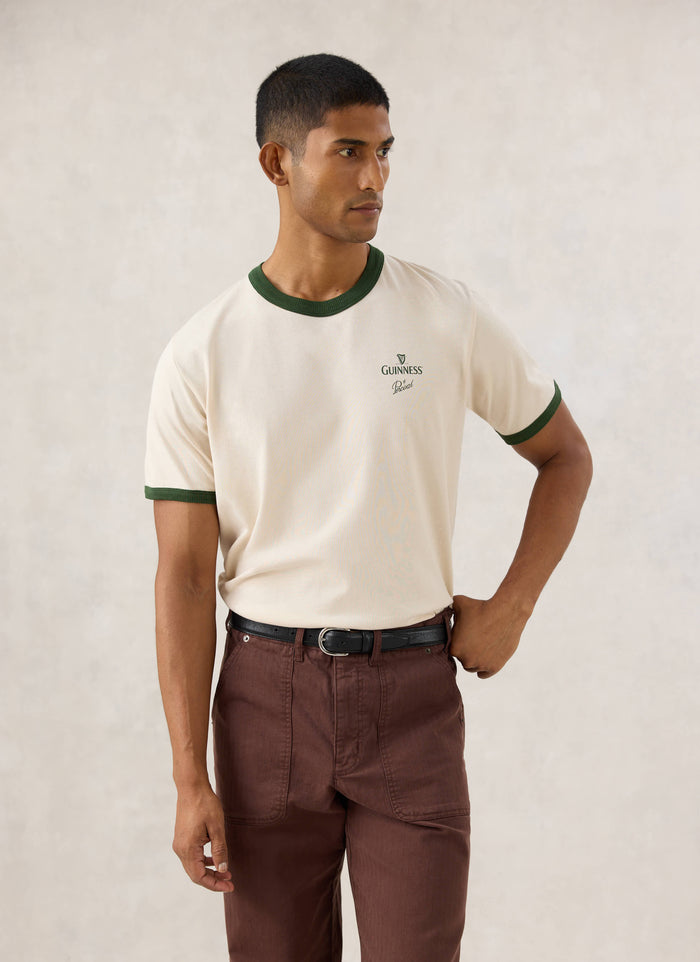 Model wearing the cream Guinness x Percival ringer T-shirt featuring forest green contrast trim and chest branding.