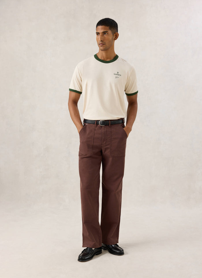 Pranav wearing the Guinness x Percival cream ringer T-shirt with forest green trim, styled with brown trousers.
